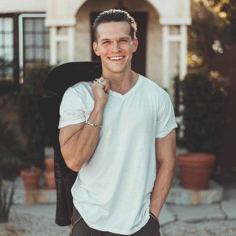 Joyful man standing in front of a house, depicting the happiness and stability gained from successful addiction stabilization services.