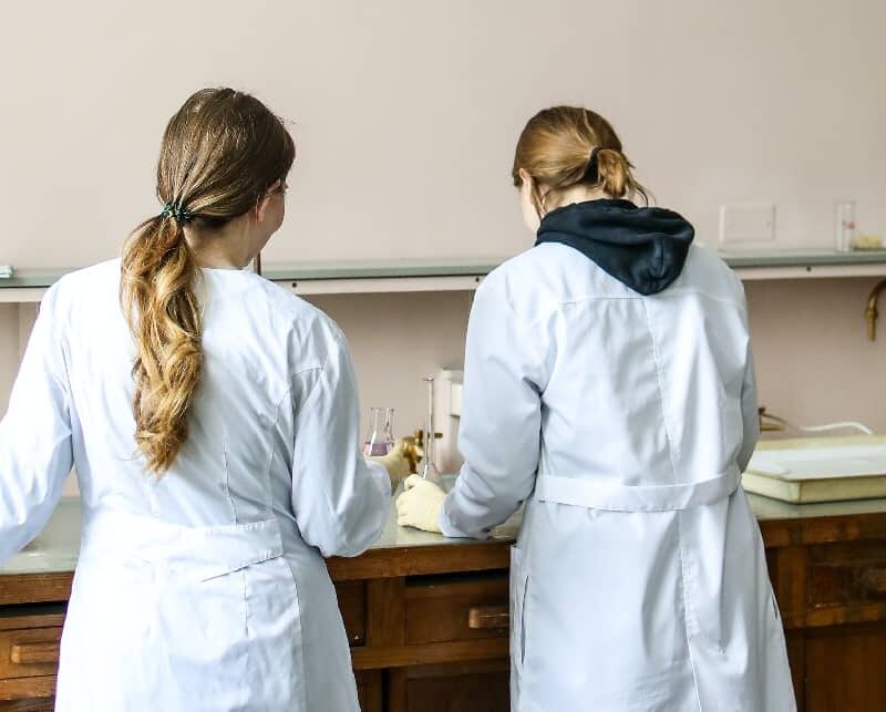 Two women wearing lab coats conducting scientific tests in a laboratory, to find out how long edibles stay in your system.