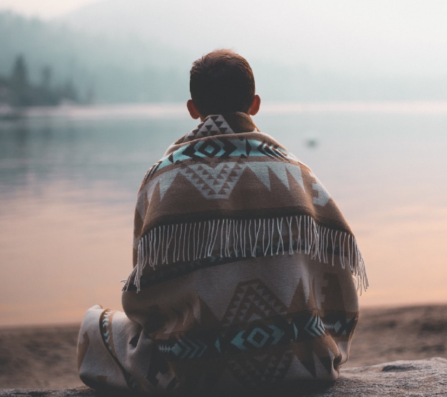 Man wrapped in a blanket, gazing into the horizon, symbolizing introspection and hope in the journey of getting amphetamine addiction treatment