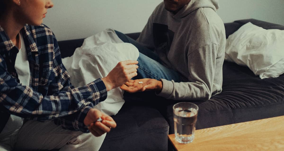A woman handing pills to a man in bed, highlighting the intimate and often hidden moments of pursuing a trazodone high