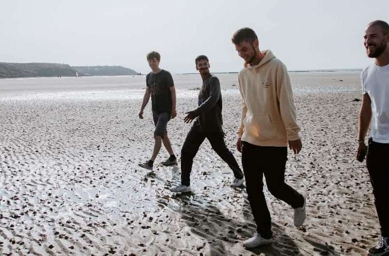 Young men walking on the beach, discussing their journey with wearable devices for recovery and sharing milestones.