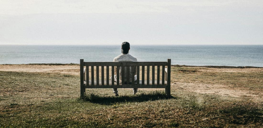 A contemplative man sitting on a bench overlooking a serene lake vista, representing reflection and the hope for recovery from crocodile drug addiction.