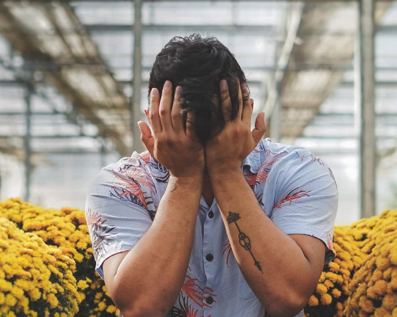 A man with a contemplative expression holds his hands over his face against a muted background, symbolizing introspection and the psychological complexities explored in the article 'What is an Acid Trip.'