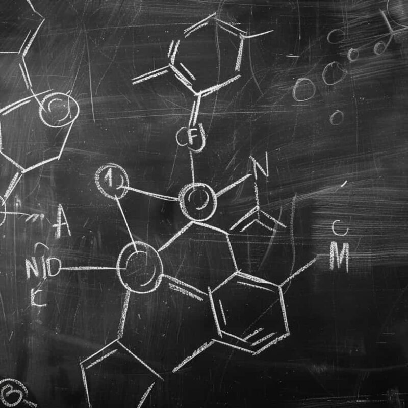 A blackboard densely covered with the detailed chemical structures of LSD, illustrating the complex process of how LSD is made.