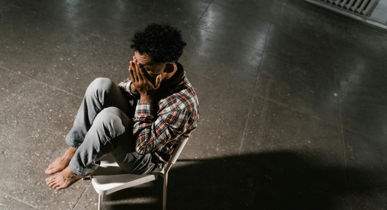 Young man sits in a chair in a big empty room with his hands covering his face to show, "how long does acid last."